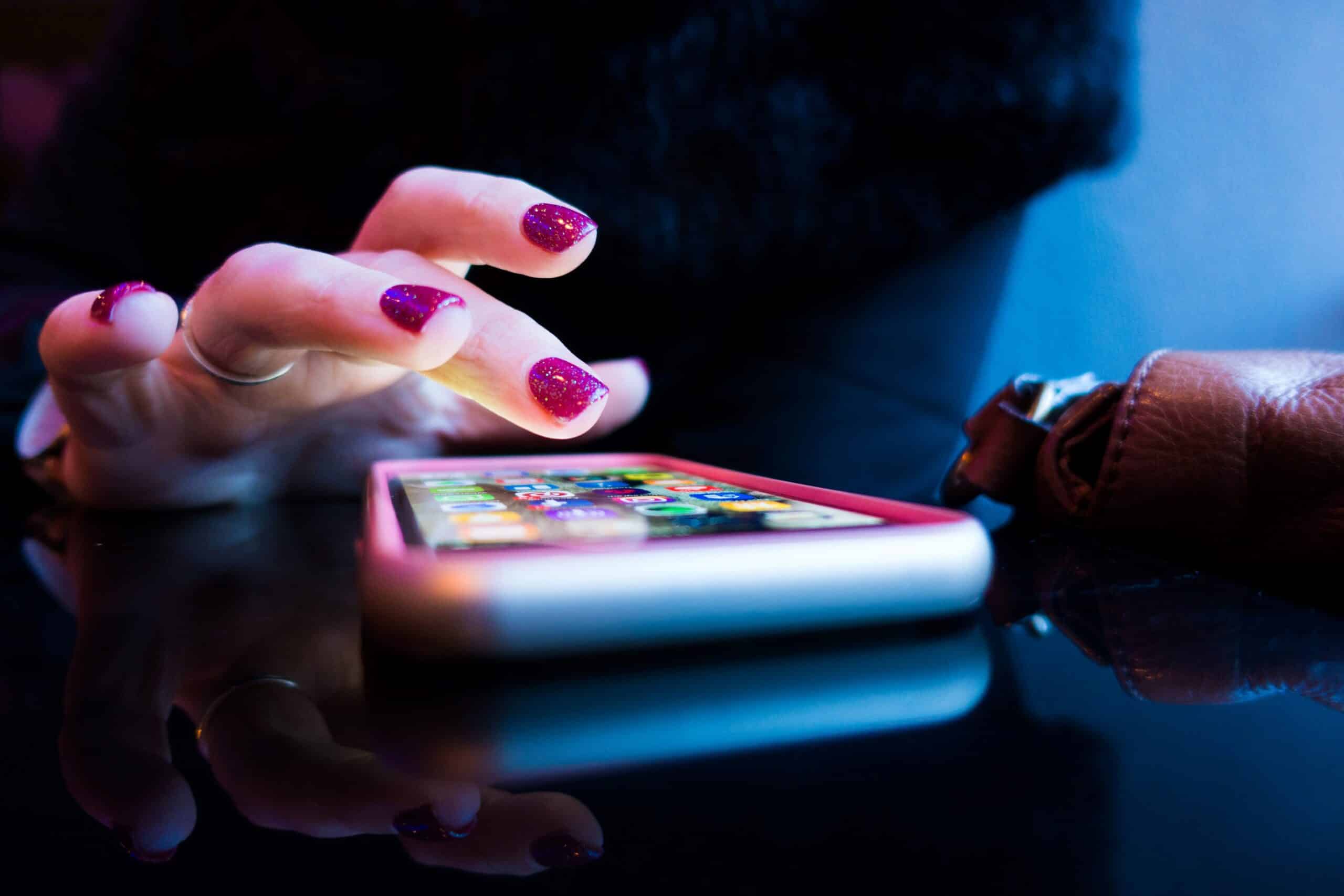 a woman's hand with pink nails touching a cell phone